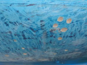 Gelcoat mit Resten des dunkelblauen Antifoulings und fast kreisrund ausgeschliffenen Osmosestellen
